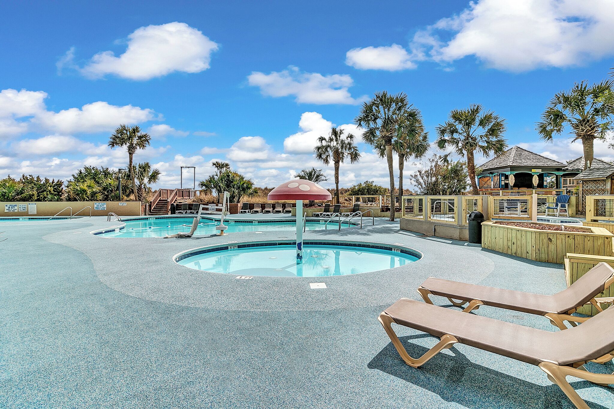 A pool area with lounge chairs and a shaded structure.