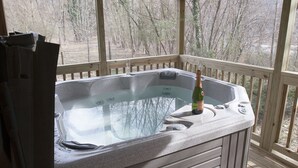 Ein Whirlpool mit einer Champagnerflasche auf einer Holzterrasse mit Blick auf Bäume.