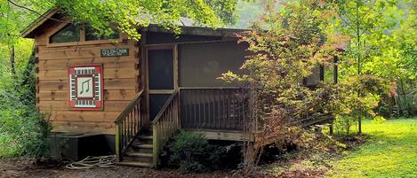 Une cabane en bois avec un escalier menant à une terrasse, le tout entouré d’une végétation luxuriante.