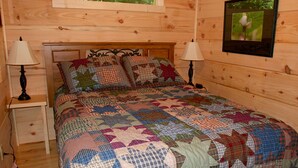 Ein Schlafzimmer einer Holzhütte mit einem Bett, zwei Nachttischen und einem gerahmten Bild an der Wand.