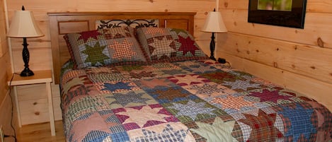 Un dormitorio de cabaña de madera con una cama, dos mesitas de noche y un cuadro enmarcado en la pared.