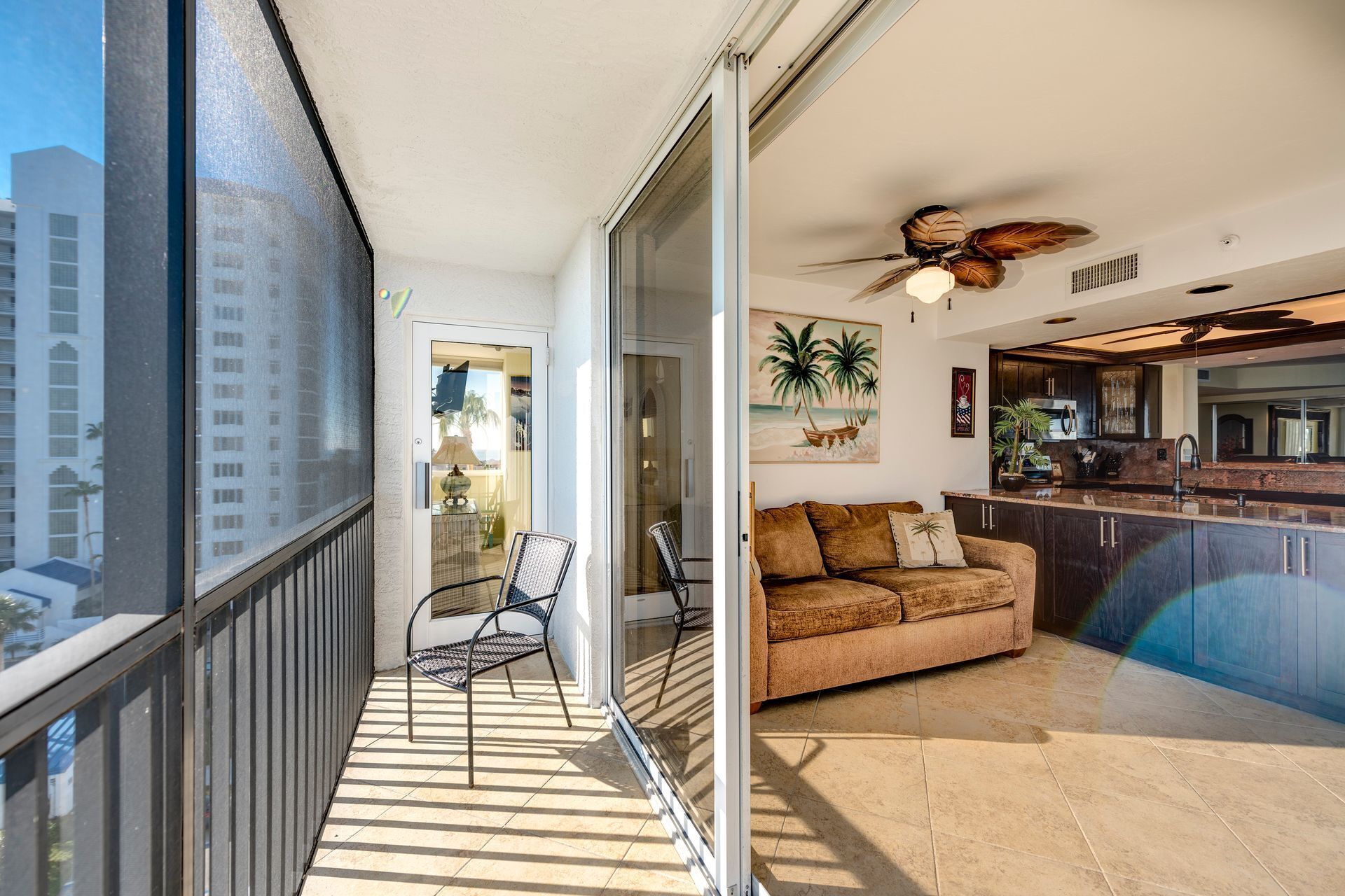 Un balcon avec une porte-fenêtre, un canapé, une chaise et un ventilateur de plafond.