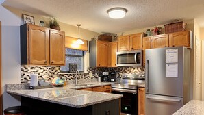 Cocina moderna con armarios de madera, encimeras de granito, electrodomésticos de acero inoxidable y una isla central con taburetes de bar.