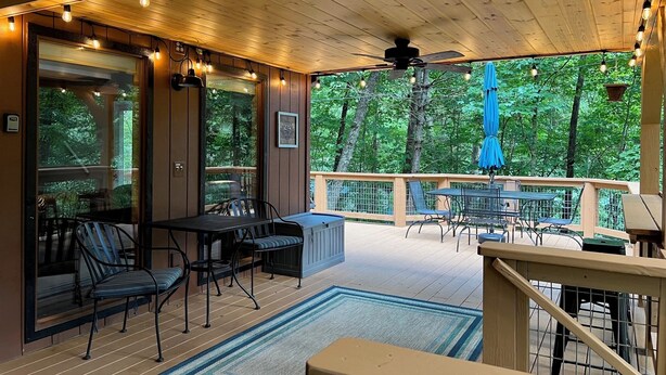 Un espacio al aire libre techado con una terraza de madera, con arreglos de asientos y vistas al bosque circundante.