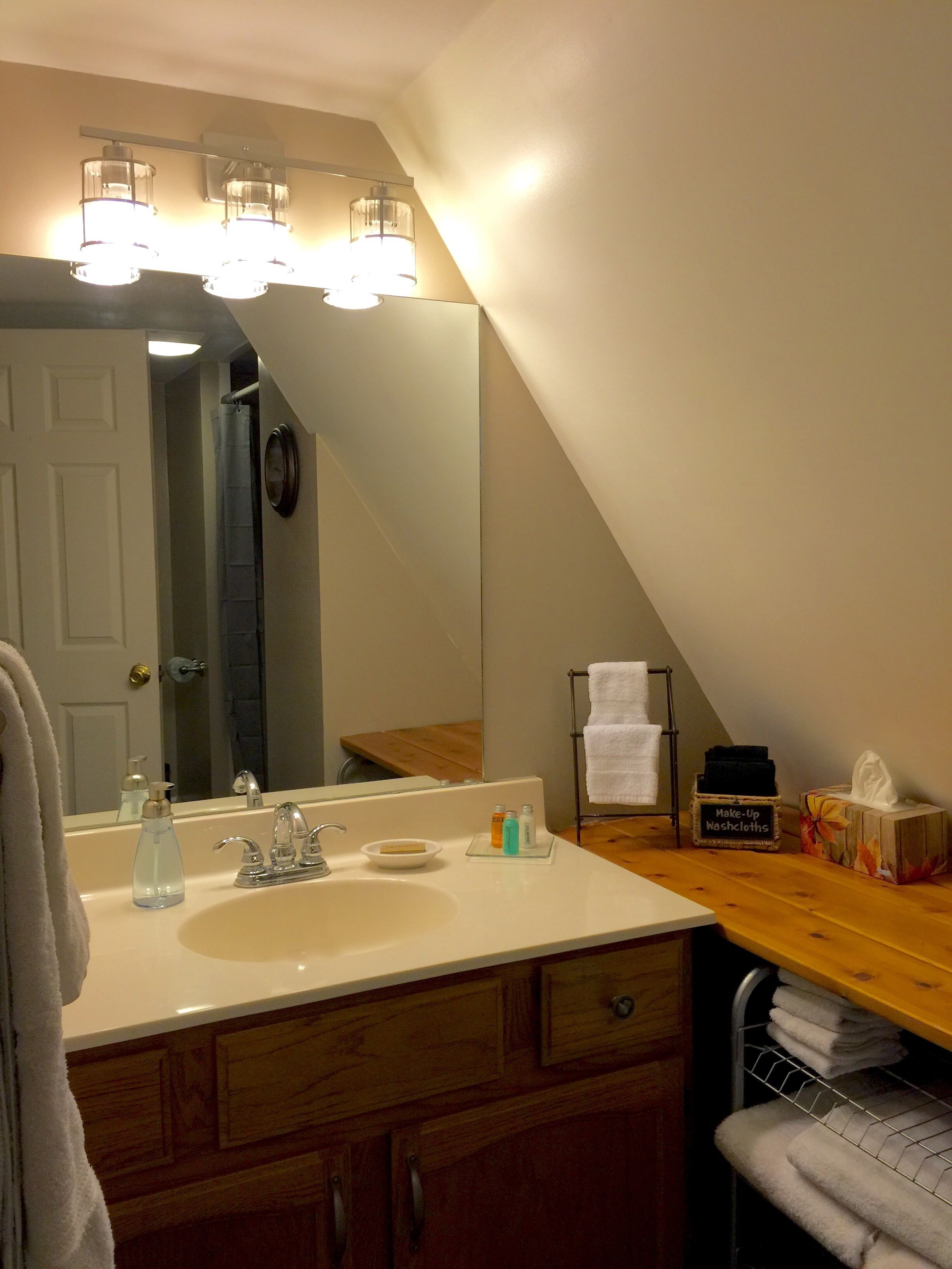 Un bagno con lavandino bianco, specchio e porta asciugamani. Sul lavandino ci sono articoli da toilette e il porta asciugamani è corredato da asciugamani piegati.