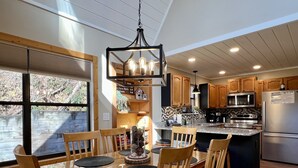 Una cocina moderna con armarios de madera, un refrigerador de acero inoxidable y una zona de comedor con mesa y sillas de vidrio.