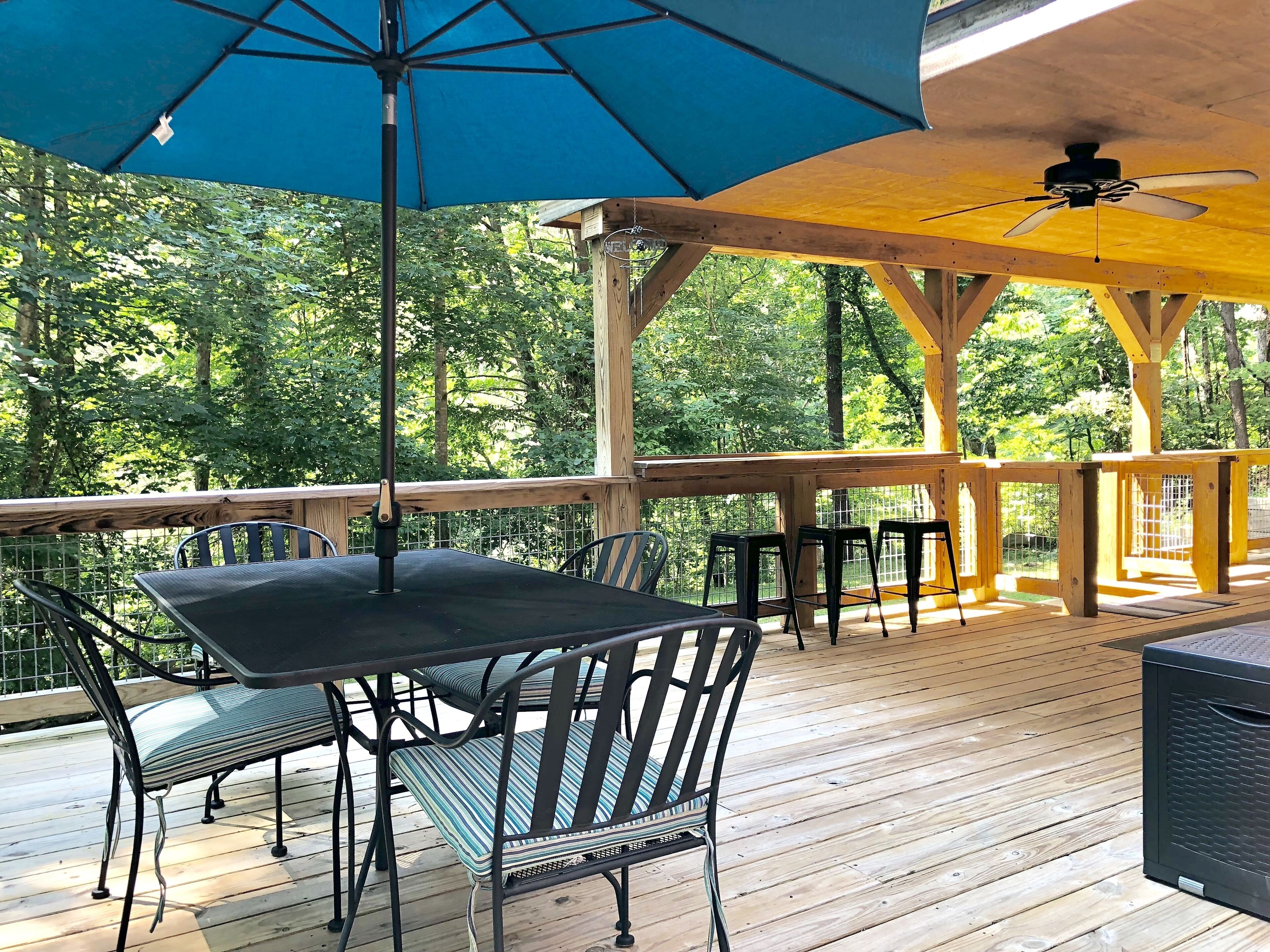 Une terrasse en bois avec une table et des chaises, un ventilateur de plafond et un parasol bleu.