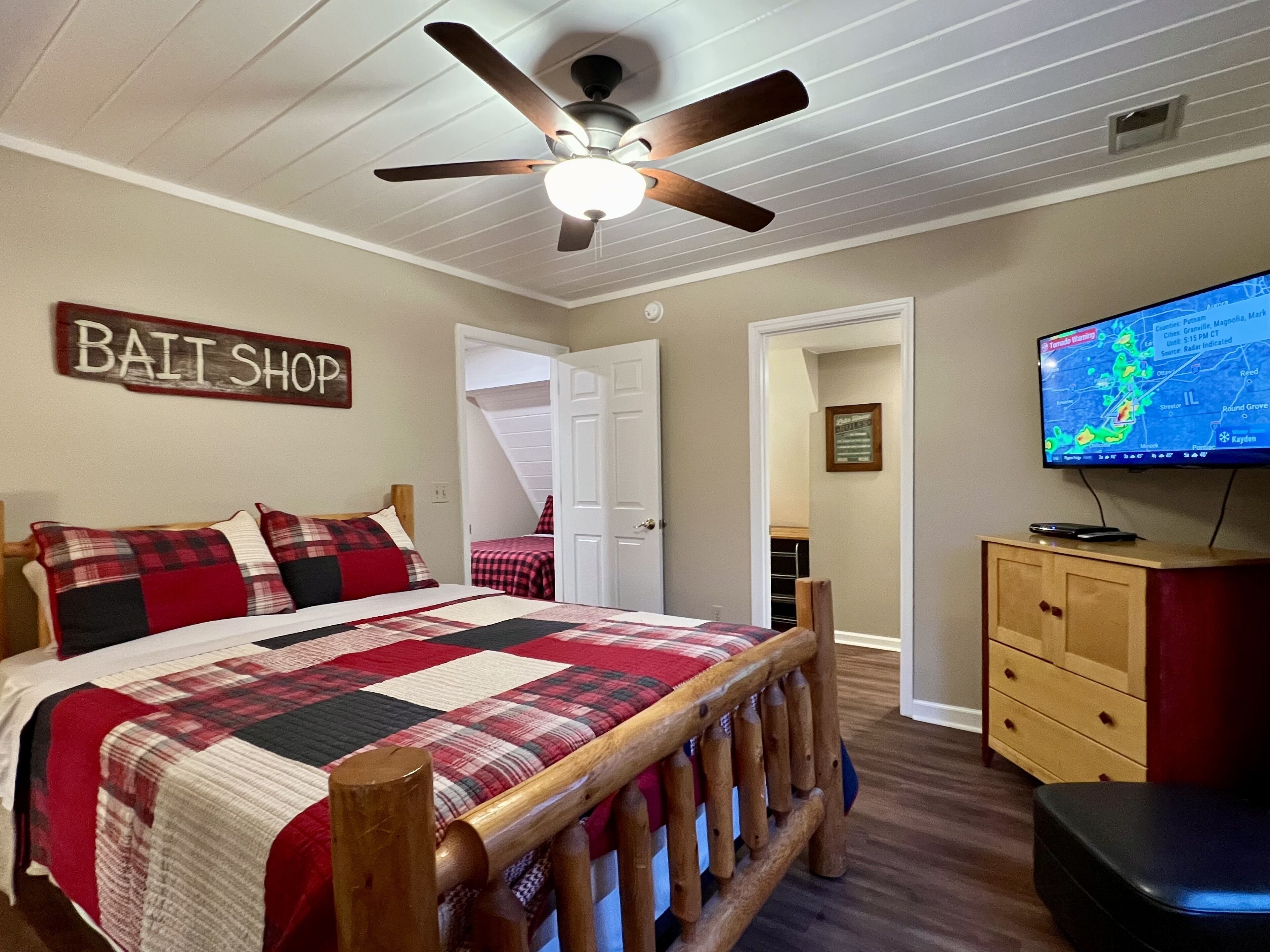 Un dormitorio con cama, ventilador de techo, televisor y un letrero que dice 'BAIT SHOP'.