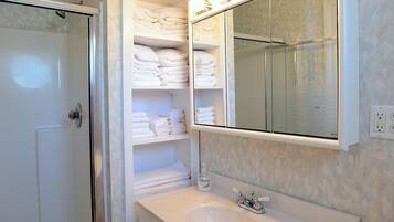 A bathroom with a walk-in shower, a large mirror, and shelves with neatly folded towels.