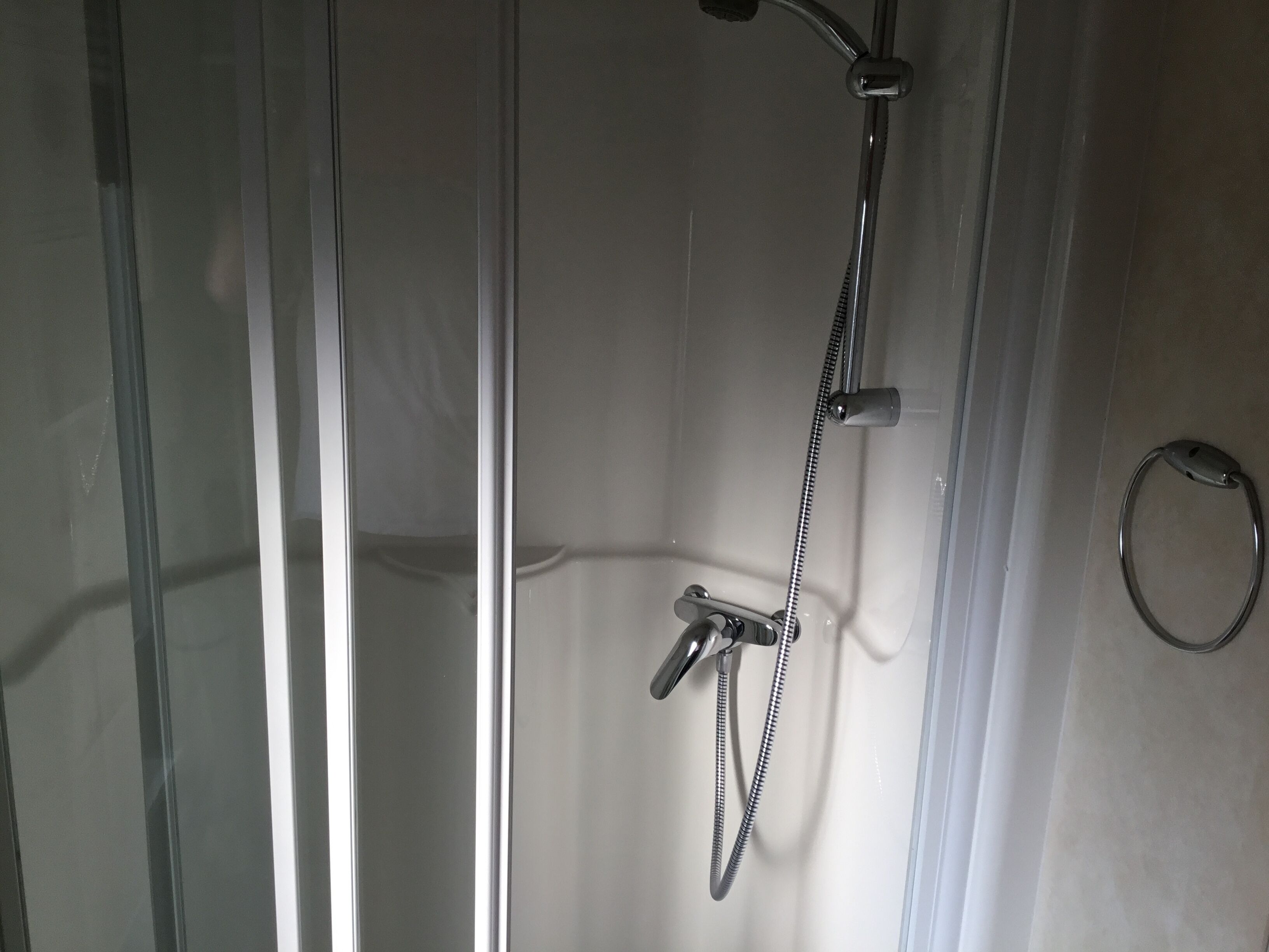 Eine Dusche mit Handbrause und flexiblen Schlauch, einem Halterung für Handtücher aus Metall und einer Glastür.