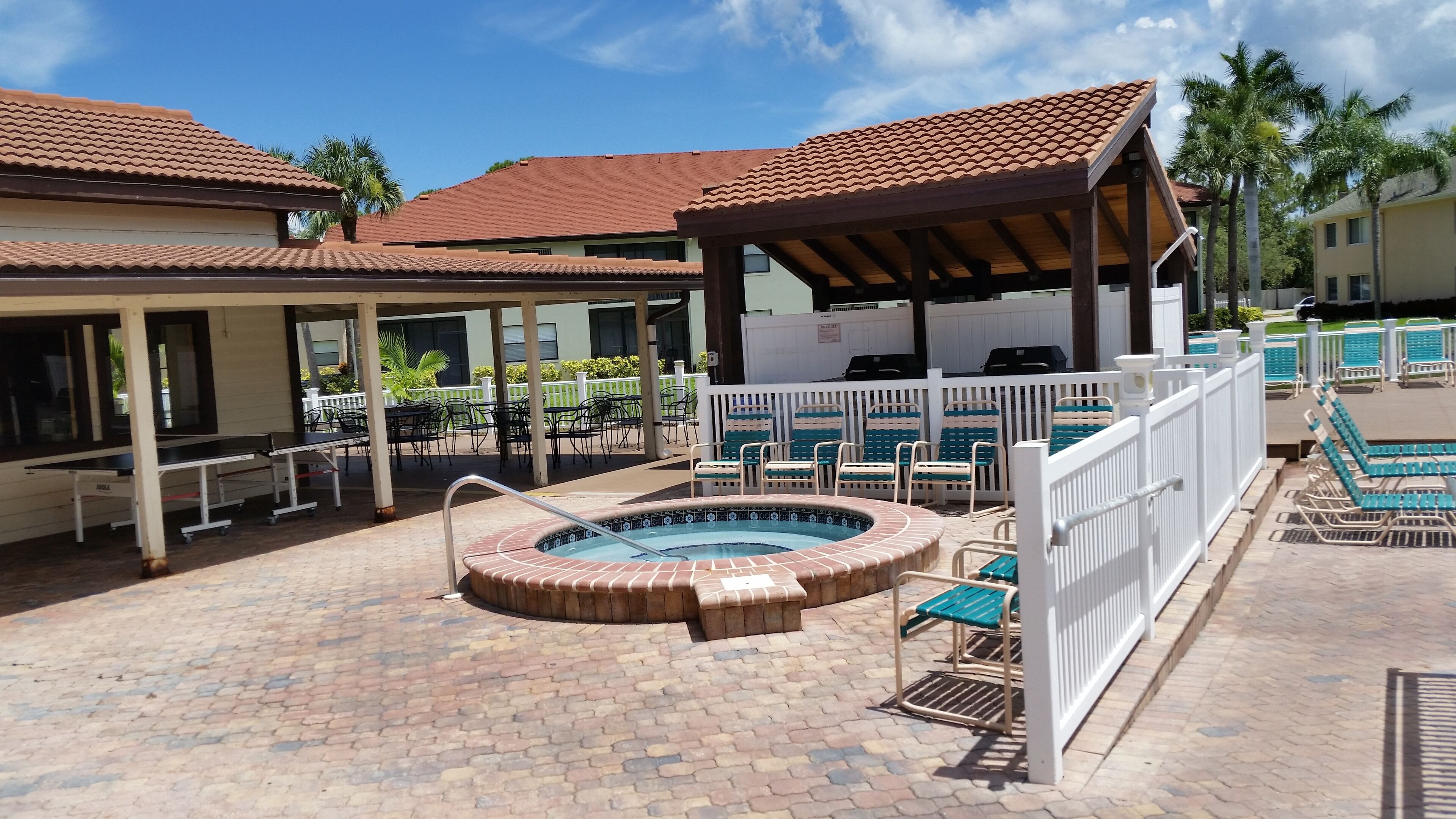 A pool area with a hot tub, lounge chairs, and a covered seating area.
