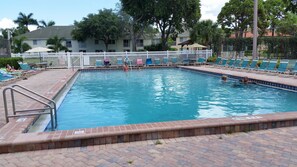 A rectangular swimming pool with a tiled edge, surrounded by lounge chairs and a white fence.