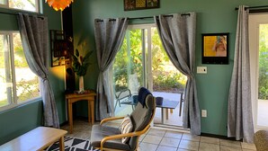 A room with a chair, a table, a hanging light fixture, and a view of the outdoors through a glass door. - Starlit Skies, 1.5 miles to Black Sand Beach, Pet Friendly, Lava Fields, Private (Pahoa)