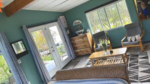 A room with a bed, a chair, a table, a dresser, and a window with a view of greenery. - Starlit Skies, 1.5 miles to Black Sand Beach, Pet Friendly, Lava Fields, Private (Pahoa)