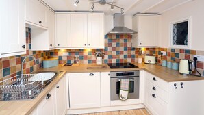 Una cocina moderna con armarios blancos, encimera de madera, horno integrado y un salpicadero de azulejos de colores.