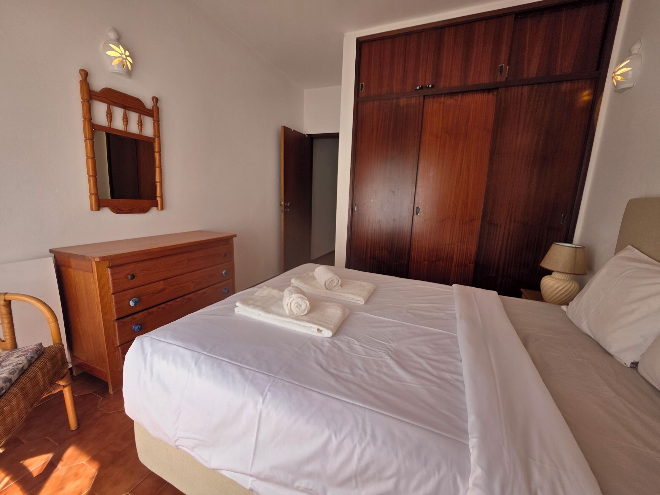 Quarto com cama, cómoda de madeira, guarda-roupa e espelho.