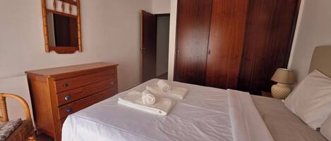 Quarto com cama, cómoda de madeira, guarda-roupa e espelho.