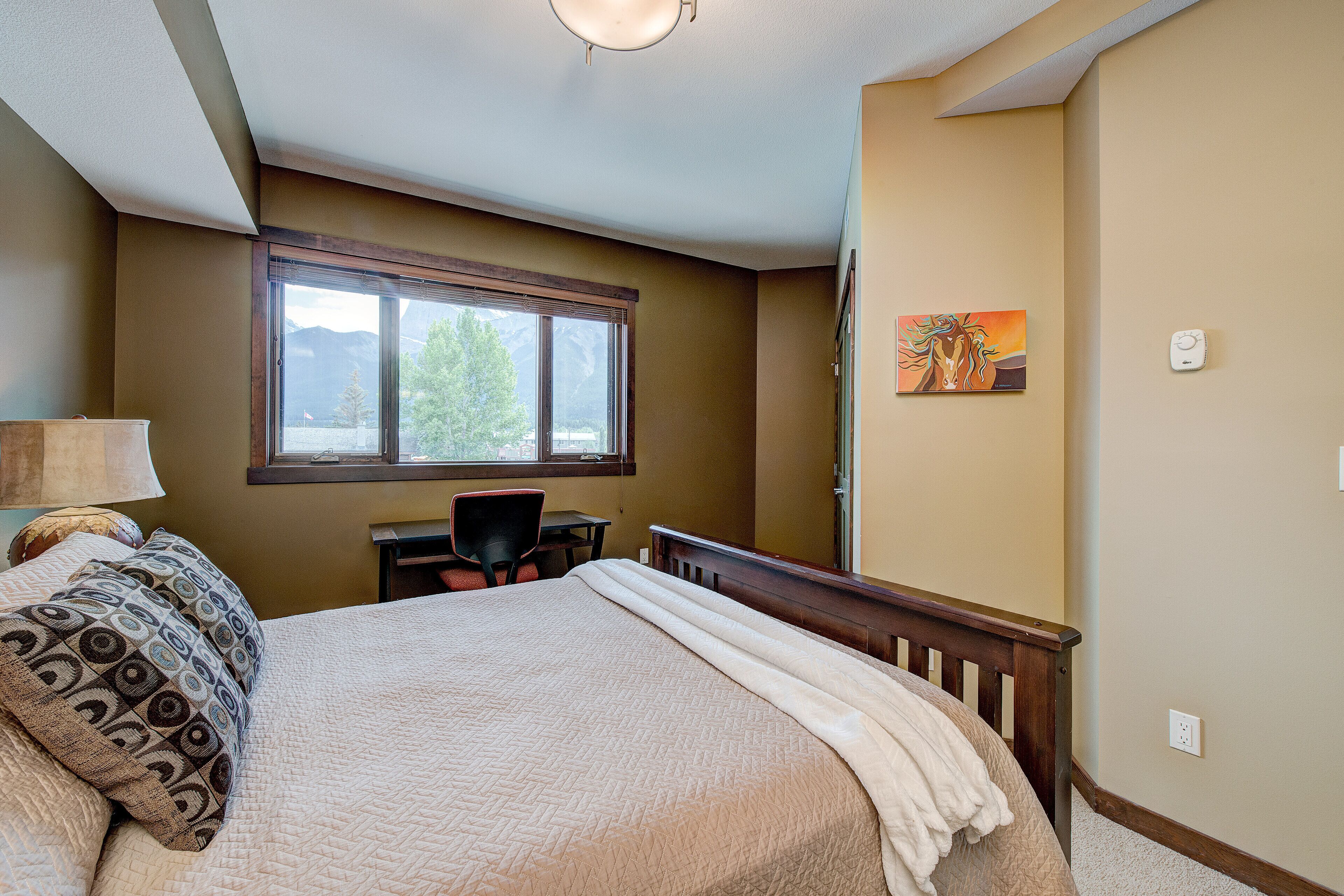 A bedroom with a large bed, a desk, and a window with a view of mountains.