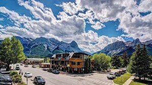 A mountain town with a prominent building in the center, surrounded by parked cars and trees. - Canmore Luxury Condo - Panoramic Mountain Views - Prime Downtown Location (Canmore)