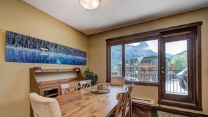 A dining area with a wooden table, chairs, and a painting of a snowy landscape. - Canmore Luxury Condo - Panoramic Mountain Views - Prime Downtown Location (Canmore)