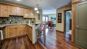 A spacious kitchen with wooden cabinets, a tiled backsplash, and a central island with bar stools. - Canmore Luxury Condo - Panoramic Mountain Views - Prime Downtown Location (Canmore)