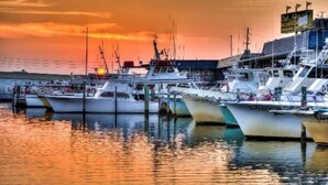 Un puerto deportivo con varias embarcaciones amarradas, un edificio con un cartel y un atardecer al fondo.