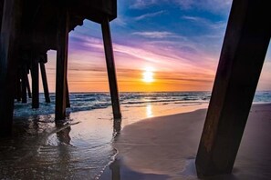 A beach scene with a sunset, featuring wooden structures that could be part of a pier or beachside building.
