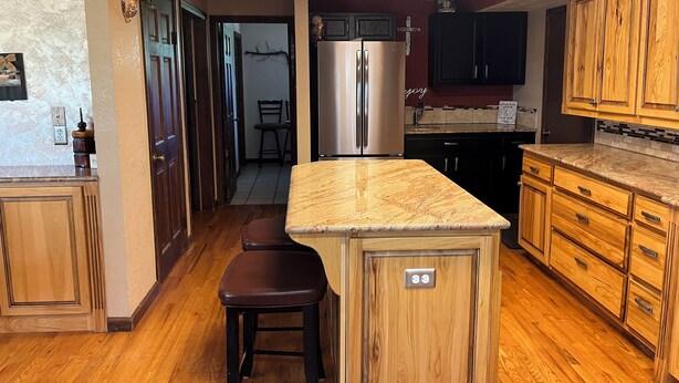 A kitchen with wooden cabinets, a stainless steel refrigerator, and a marble countertop. - 5-bedroom vacation home Mead,Co. /Easily access I-25 DenverBoulderFtCollinsEstes (Mead)