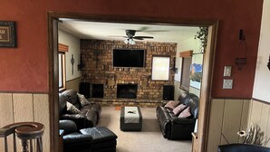 A living room with a stone fireplace, leather sofas, a flat-screen TV, and a ceiling fan. - 5-bedroom vacation home Mead,Co. /Easily access I-25 DenverBoulderFtCollinsEstes (Mead)