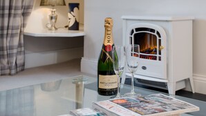 Una botella de champán Moët, dos copas y una revista sobre una mesa de vidrio en una habitación con chimenea.