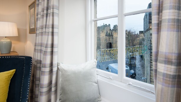 Una habitación con una cama, una ventana que ofrece vistas a un castillo, una lámpara y una cortina.