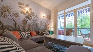 Een woonkamer met een bank, gestreepte kussens, een salontafel en een muurschildering van tropische planten.