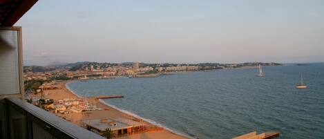 A coastal cityscape with a beach, boats, and a distant mountain range.