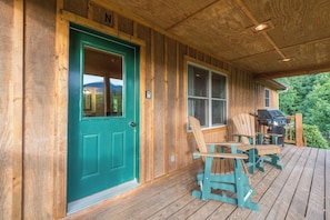 A wooden cabin with a green door, a porch with Adirondack chairs, and a grill. - Hot Tub+Fire Pit, Grill, Fireplace, WiFi, Private! (Burnsville)