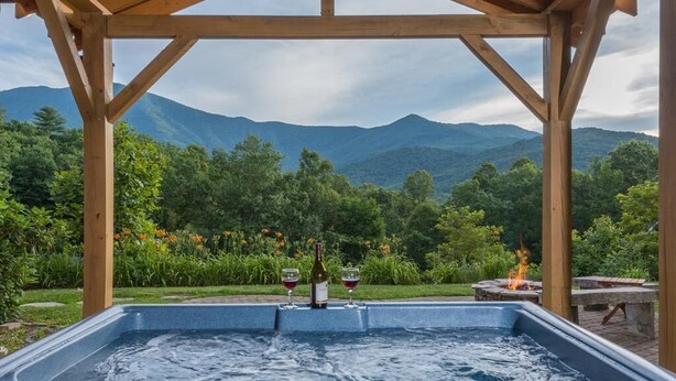 Ein Whirlpool mit einer Holzpergola, umgeben von üppiger Vegetation und Bergen im Hintergrund.