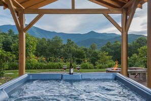 A hot tub with a mountain view, surrounded by a wooden pergola.