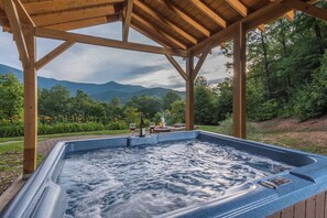 A hot tub under a wooden pergola with a mountainous landscape in the background. - Hot Tub+Fire Pit, Grill, Fireplace, WiFi, Private! (Burnsville)