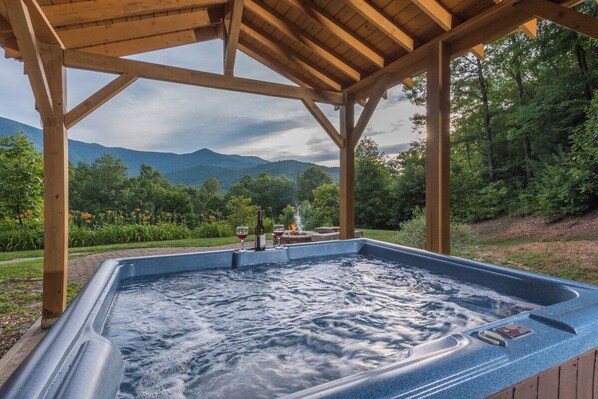 A hot tub under a wooden pergola with a mountainous landscape in the background.