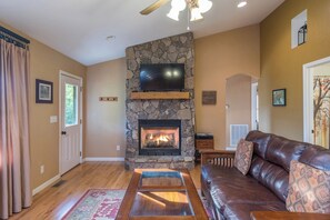 Una sala de estar con chimenea de piedra, sofá de cuero y televisor de pantalla plana.
