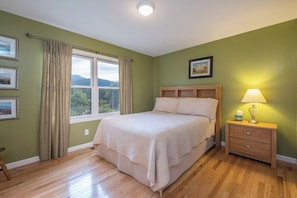 A bedroom with a bed, a nightstand, a window with curtains, and a picture on the wall.
