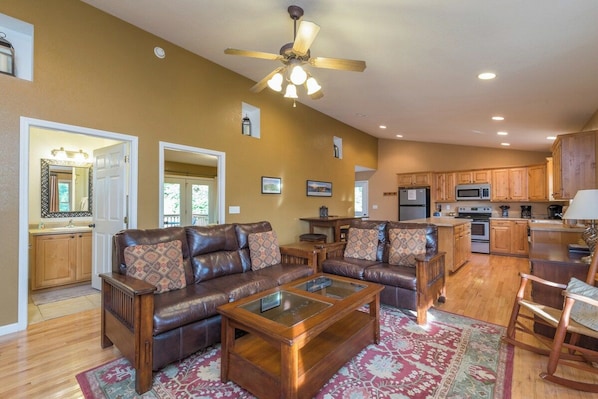A spacious living room with a brown leather sofa, a wooden coffee table, and a ceiling fan. - Hot Tub+Fire Pit, Grill, Fireplace, WiFi, Private! (Burnsville)