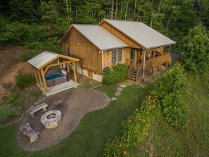 A wooden cabin with a covered patio, a hot tub, and a fire pit. - Hot Tub+Fire Pit, Grill, Fireplace, WiFi, Private! (Burnsville)