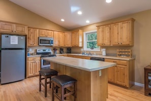 A kitchen with wooden cabinets, a refrigerator, a microwave, an oven, a sink, and a window.