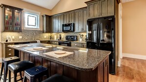 Cozinha moderna com armários de madeira escura, bancada de granito e eletrodomésticos de aço inoxidável.