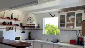 A kitchen with white cabinets, a microwave, a stove, and a window with a view of greenery. - Sugar Cane House (GRAND BOURG)