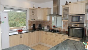 A modern kitchen with wooden cabinets, a built-in stove, a microwave, and a coffee maker. - House / Villa - Porto vecchio (Porto-Vecchio)