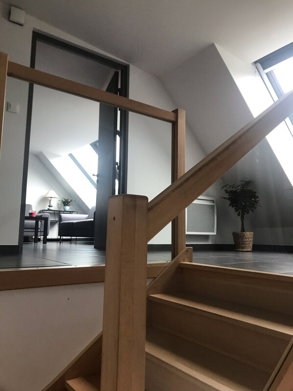 A wooden staircase leading to a loft bedroom with skylights, a TV, and a potted plant.