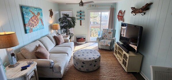 Un salon comprenant un canapé, un pouf, un téléviseur et des objets de décoration.
