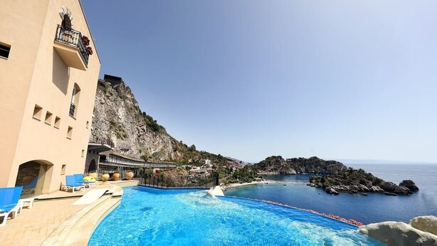 A pool area with a view of the sea and a building with a balcony. - Villette Taormina, La Perla Dell'isola (Taormina)