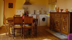 Een kleine keuken met houten kastjes, een wasmachine en een eethoek met houten stoelen.